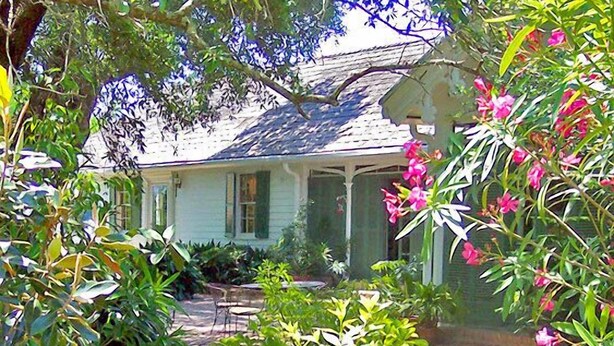A house with a covered porch, surrounded by lush greenery and flowering plants.