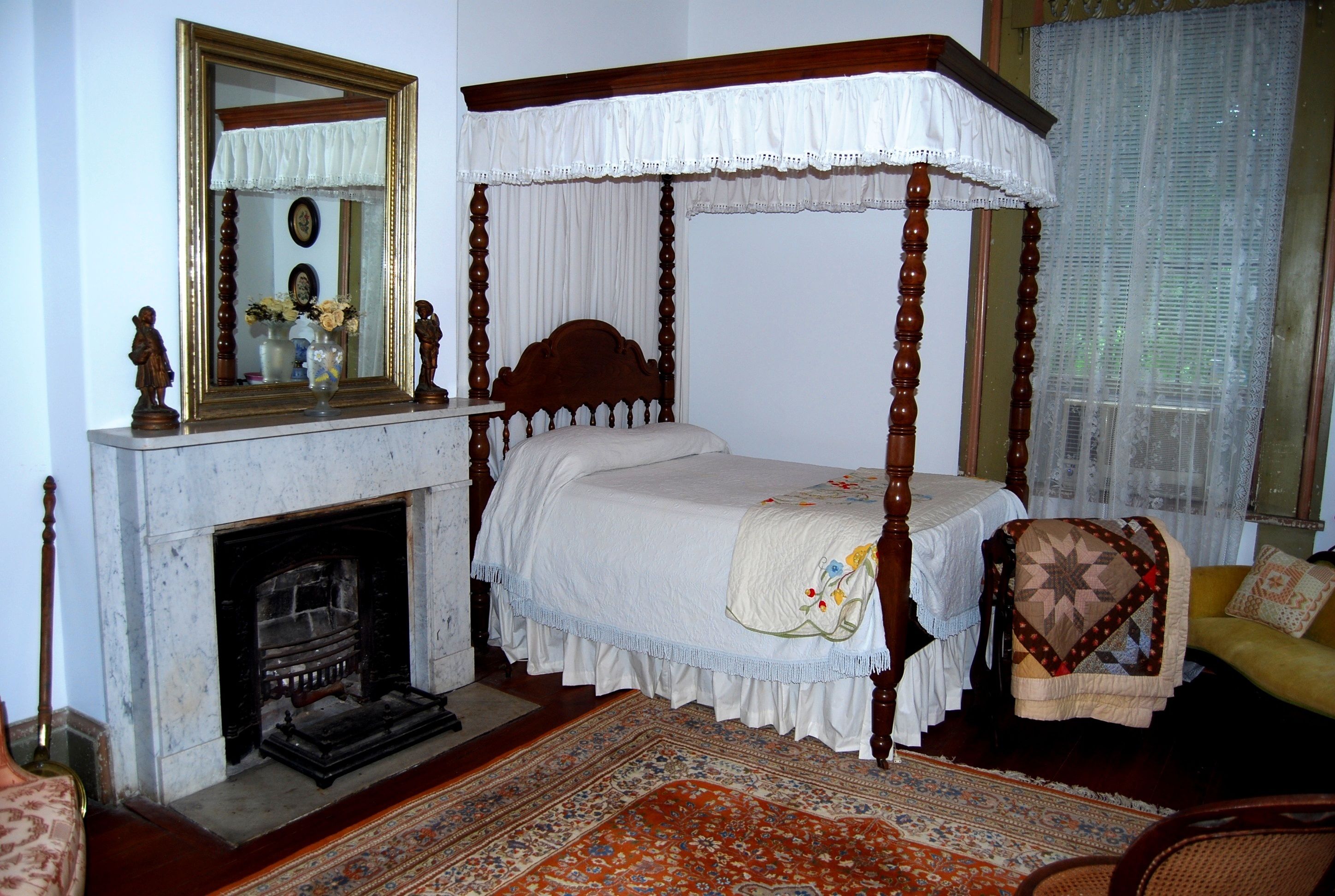 Un lit à baldaquin blanc, une cheminée, un miroir et un tapis à motifs.