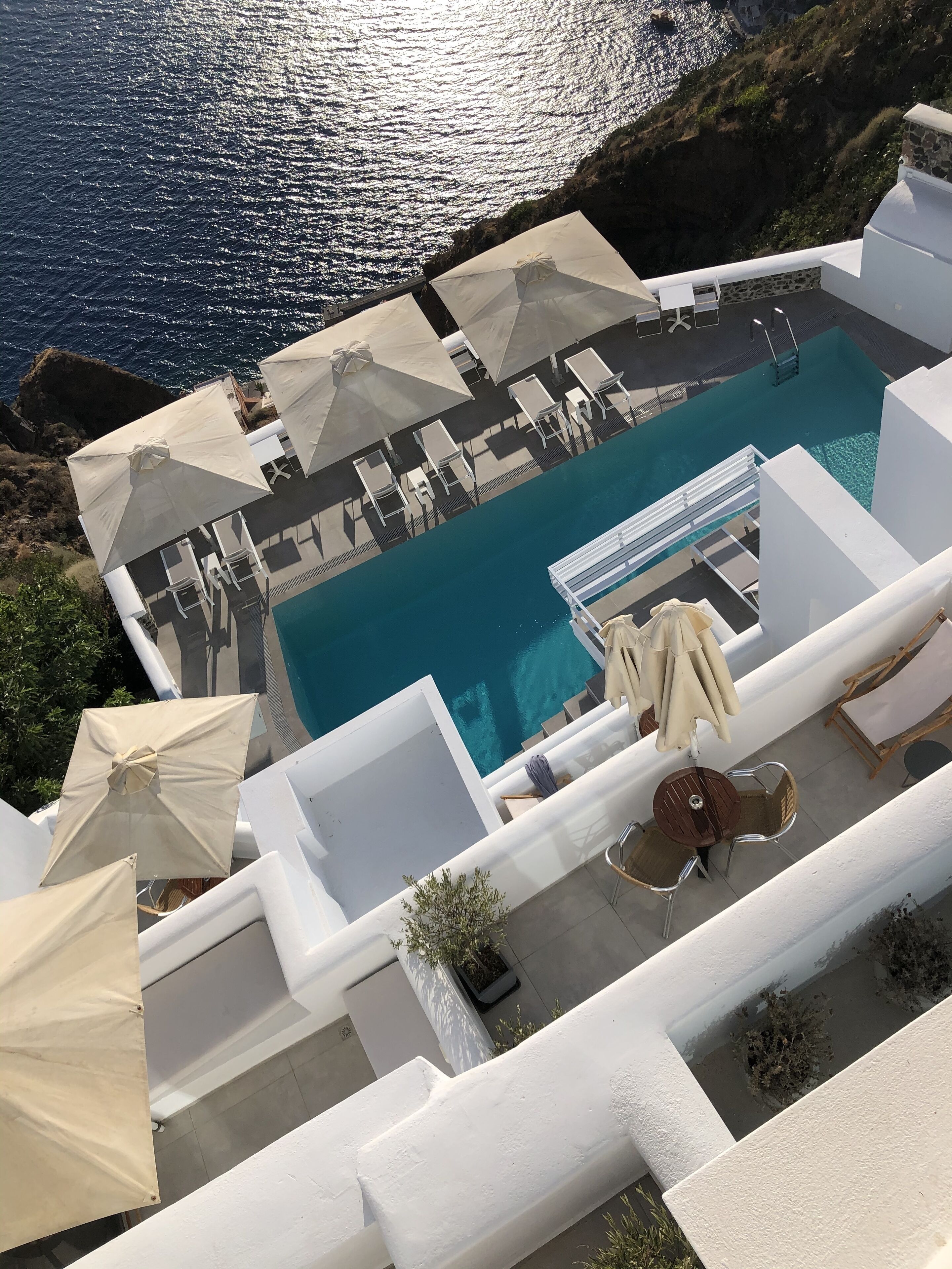 A rooftop pool with white lounge chairs and umbrellas, overlooking a body of water.