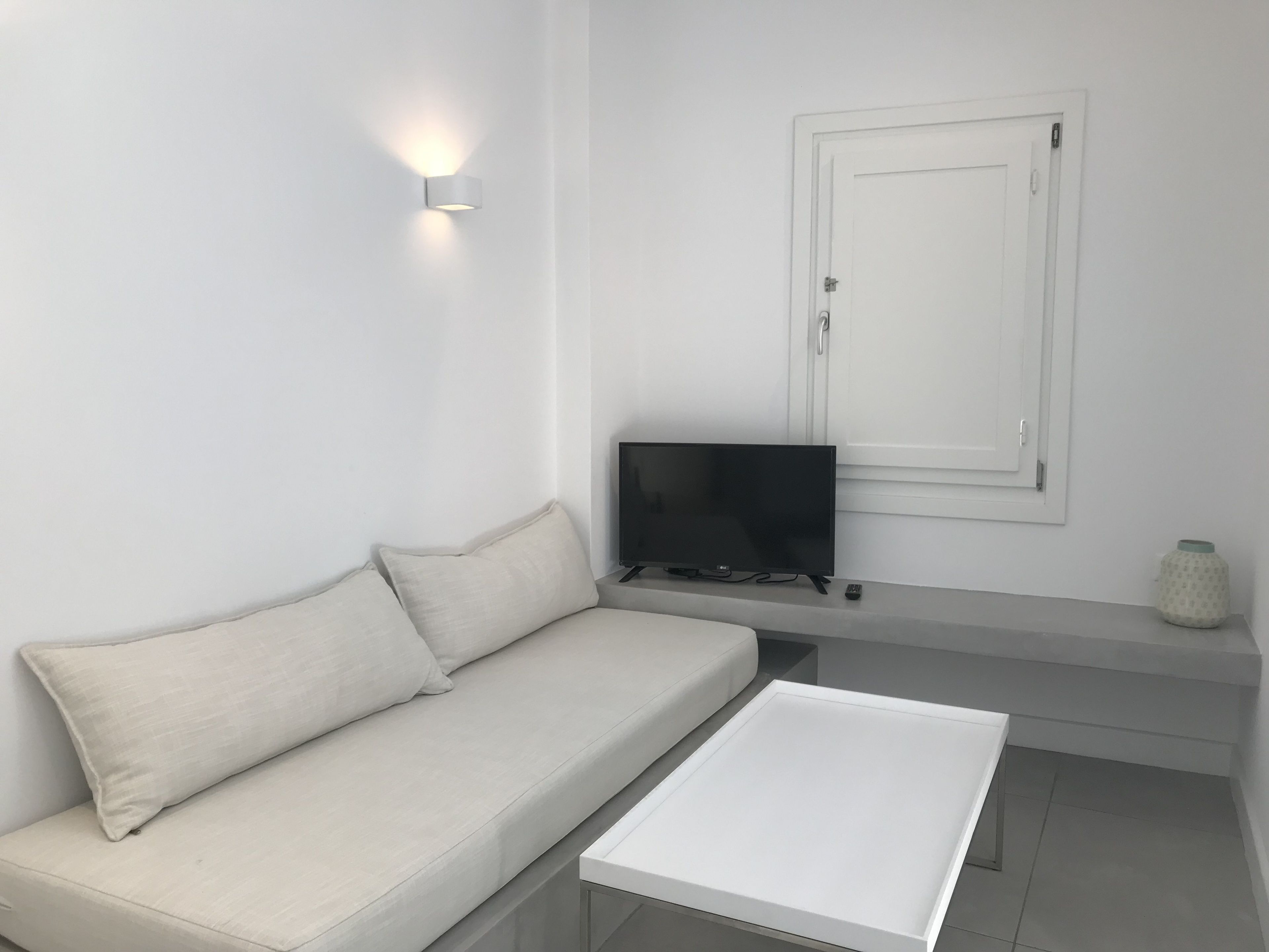 A minimalist living room with a white sofa, a flat-screen TV, and a small white table.