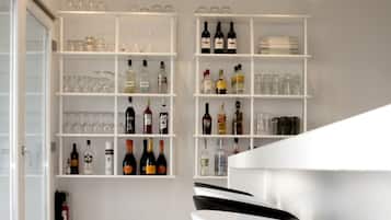 A modern bar area with white shelves stocked with bottles and glasses, a fire extinguisher, and a black bar stool.