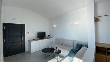Una sala de estar moderna con un sofá blanco, una mesa de centro negra y un televisor sobre un mueble de madera.