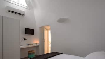 Un dormitorio minimalista con cama, televisor montado, escritorio con lámpara y puerta que da a otra habitación.
