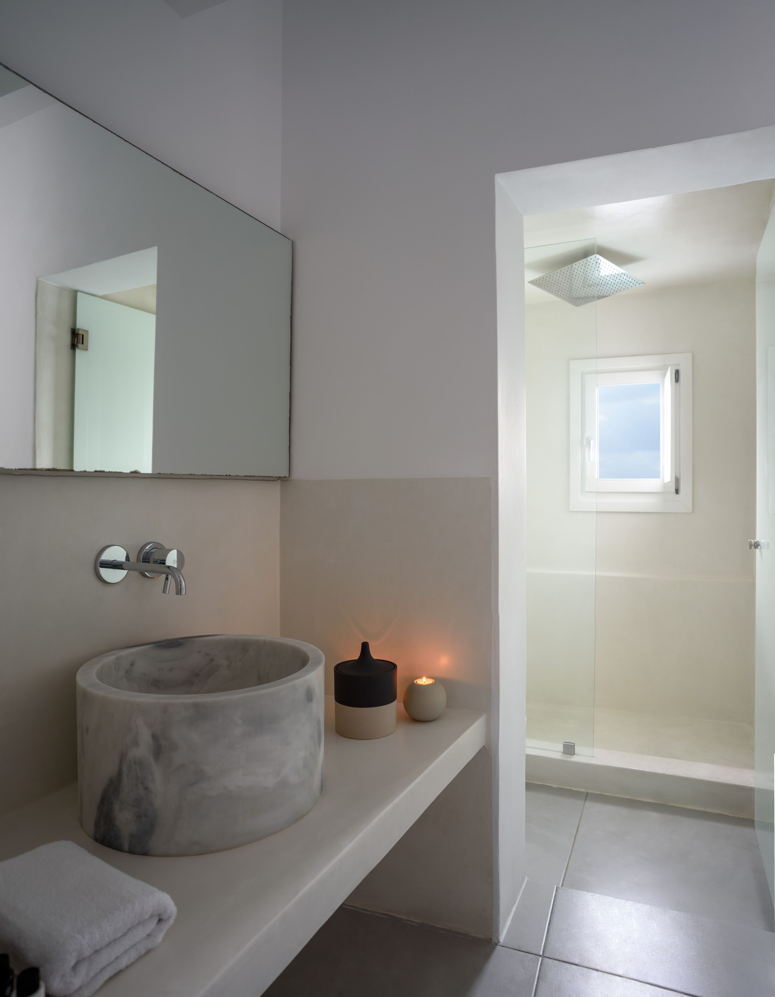 Un bagno moderno con lavabo in marmo, uno specchio, una piccola candela e l'area doccia visibile attraverso una porta aperta.