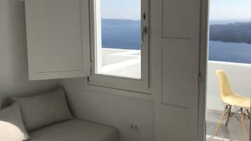 A room with a sofa, a small table, and two doors leading to a balcony with a view of the sea.