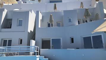 A white building with multiple balconies, a staircase, and a pool area.