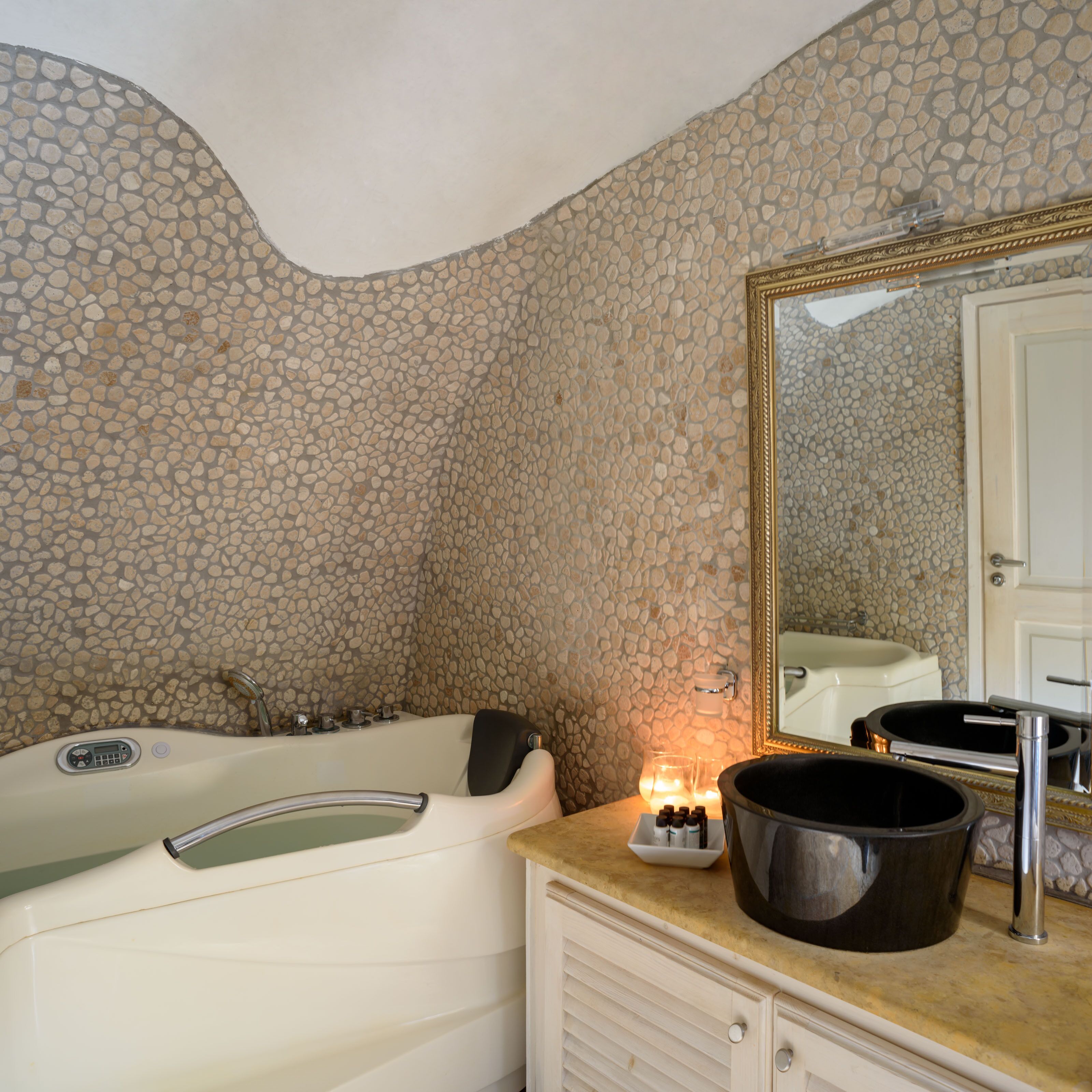 A bathroom with a stone wall, a bathtub, a mirror, and a sink with toiletries.