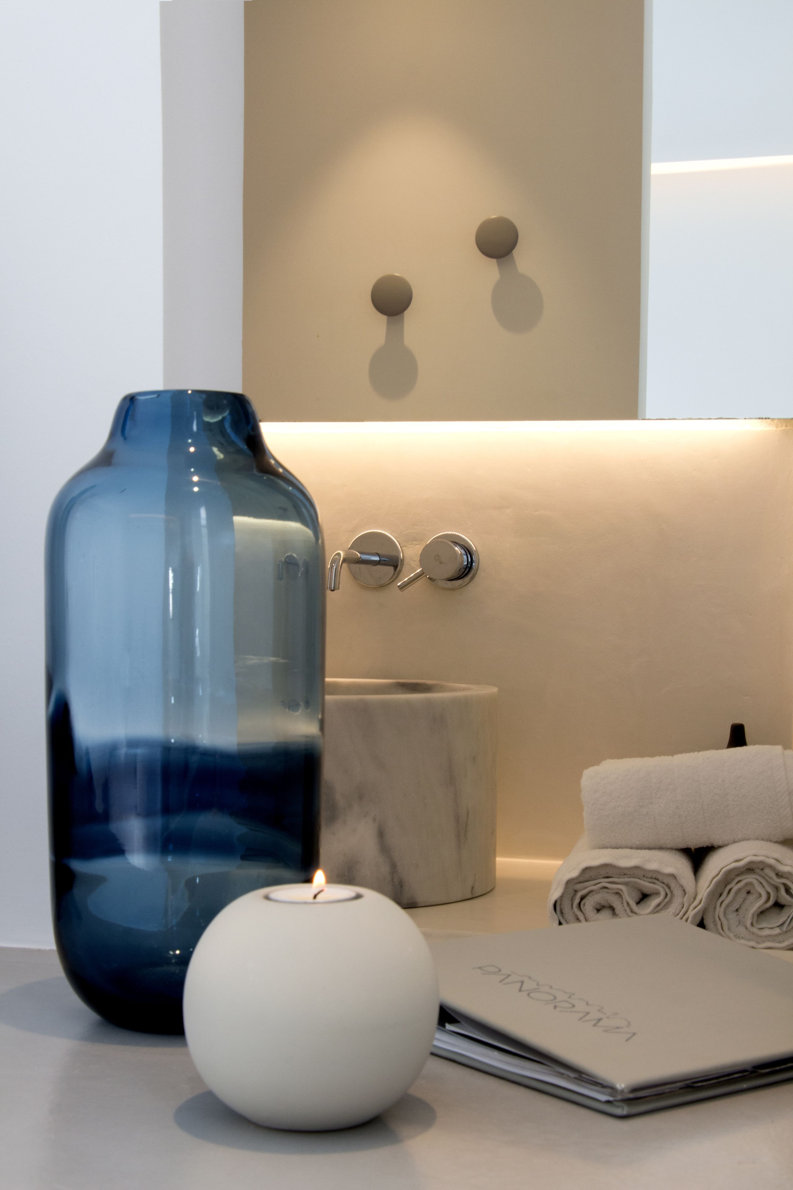 A bathroom with a large blue vase, a white candle, a marble container, and neatly rolled towels.