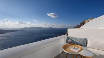 Ein Balkon mit weißer Reling und Blick auf das Meer, ein runder Tisch mit einem Glas Rotwein und ein Kissen mit geometrischem Muster.
