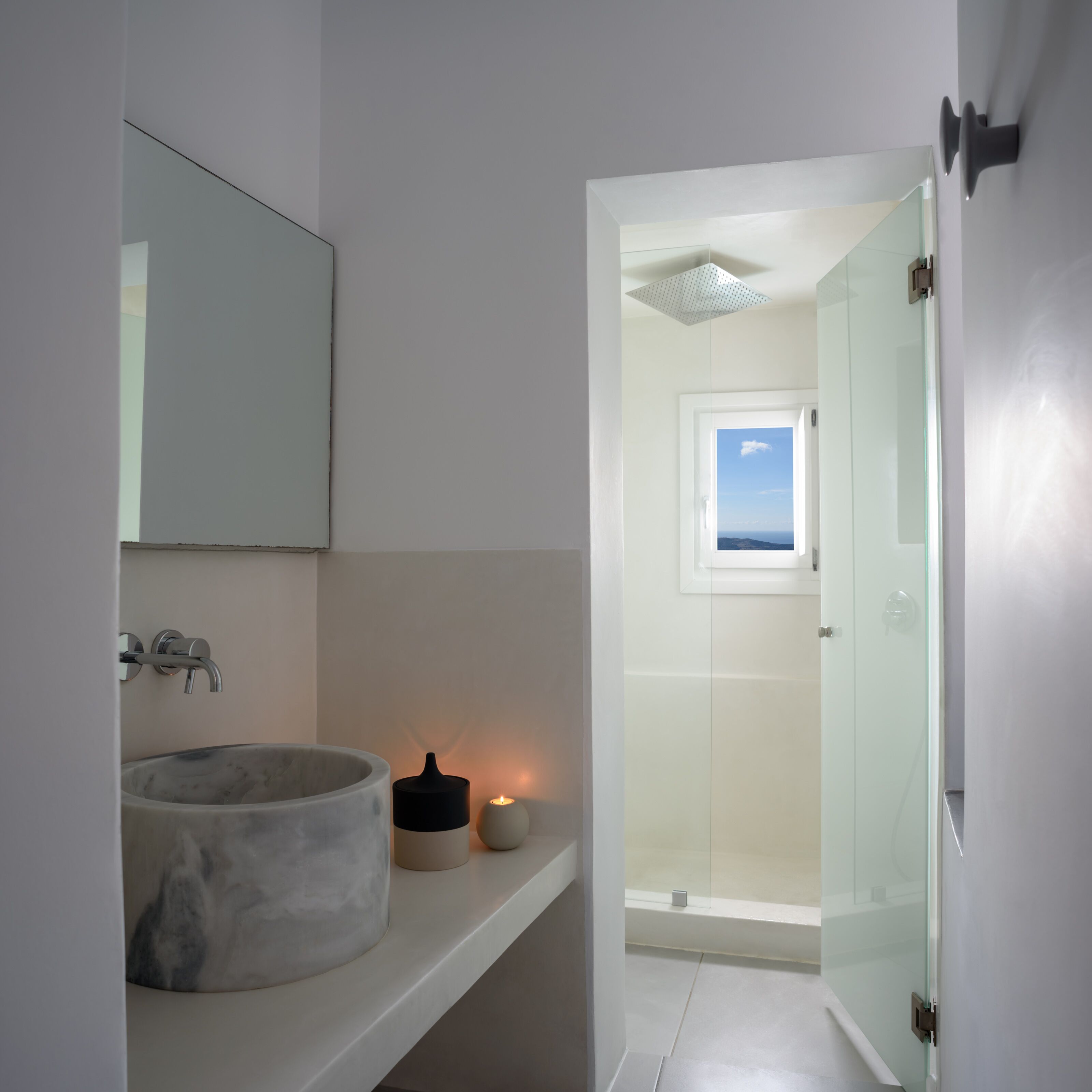 Un bagno moderno con lavabo in marmo, una piccola candela e box doccia in vetro.