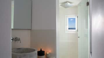 Un baño moderno con un lavamanos de mármol, una vela pequeña y un box de ducha de vidrio.