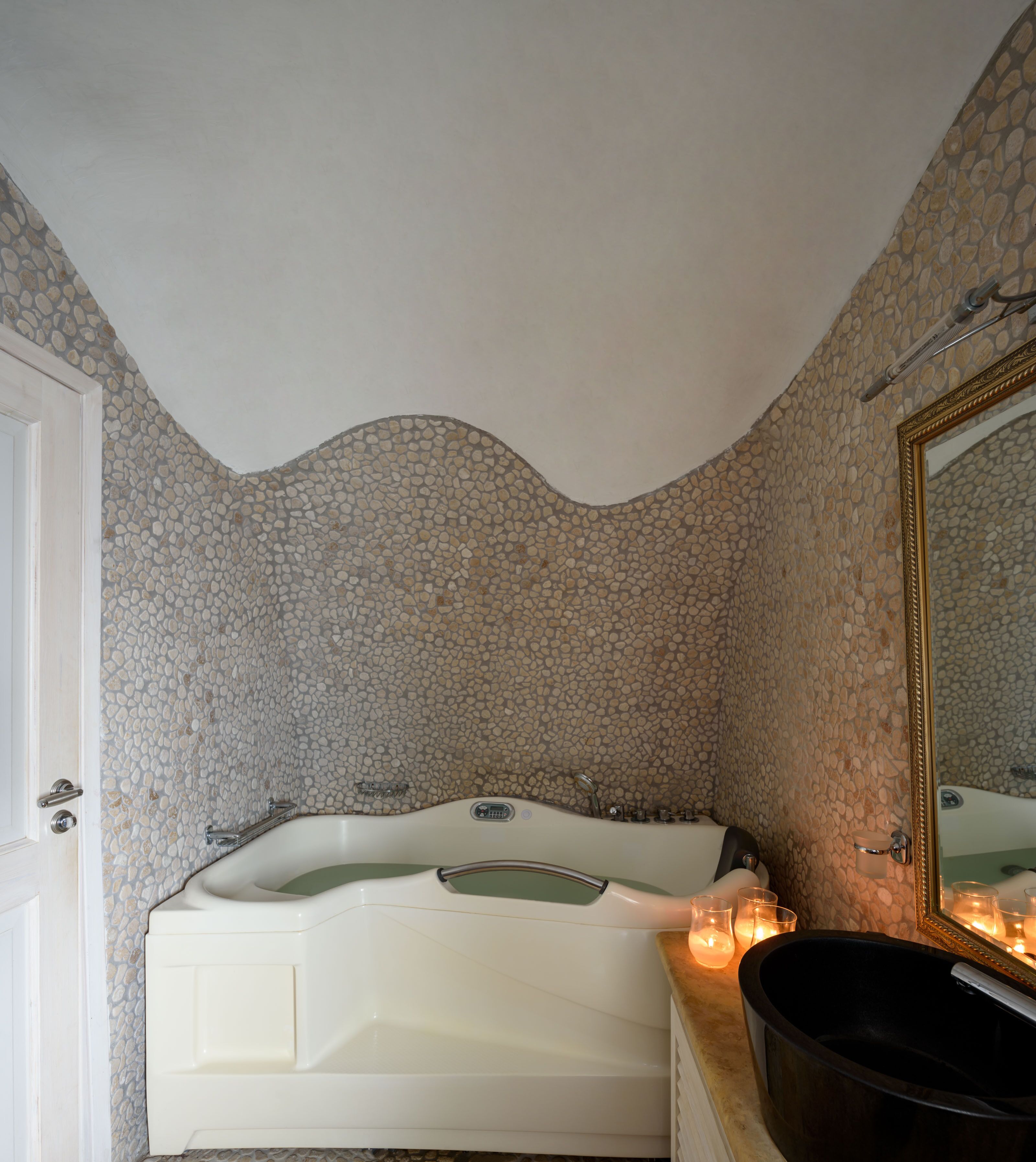 Ett badrum med en vägg täckt av ett stenmosaikmönster, ett vitt badkar och en stor spegel.