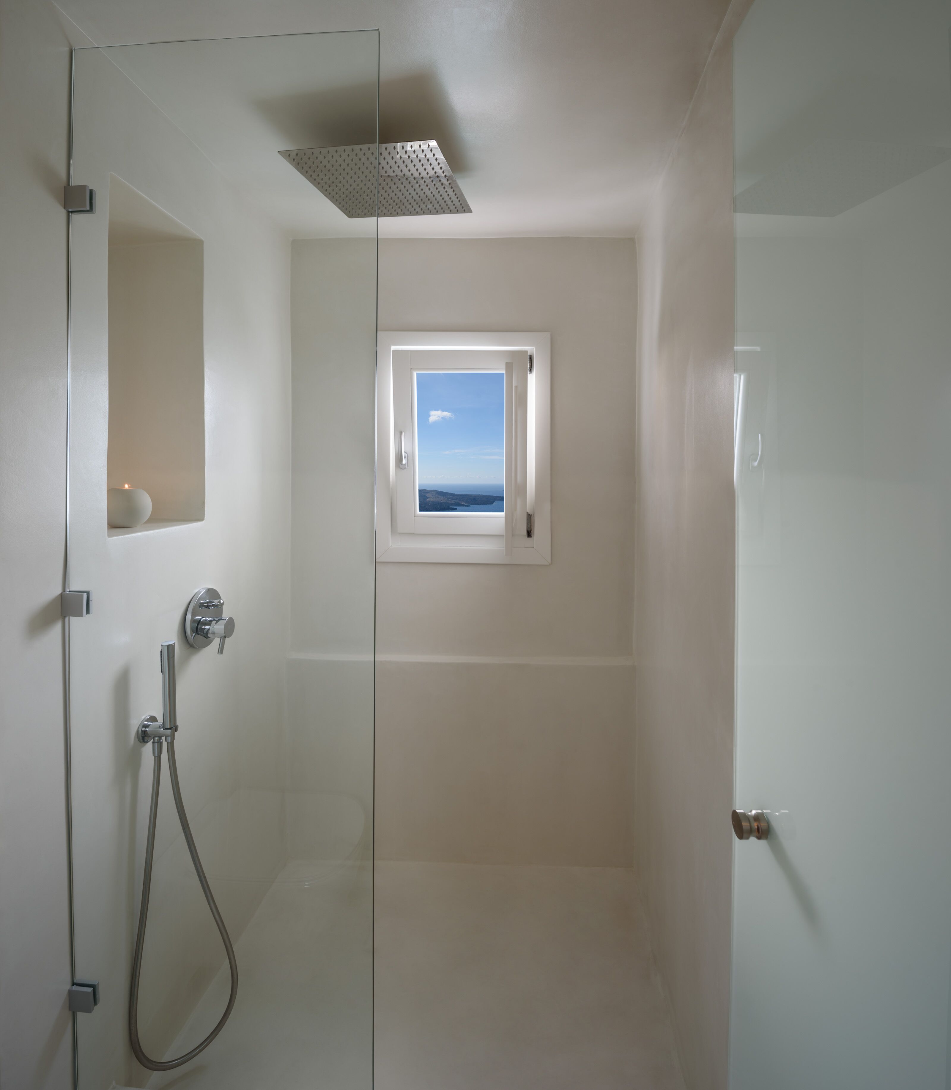 A shower with a glass door, a small window, and a view of the sea.