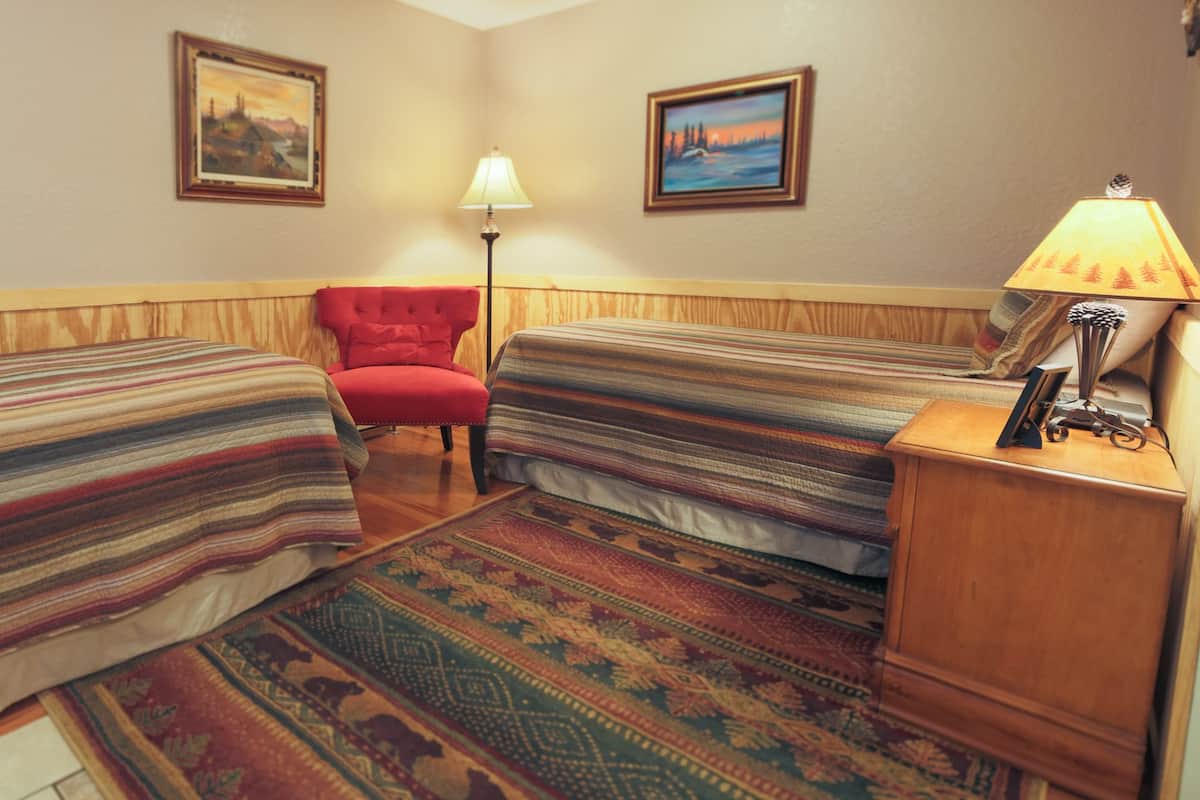 A hotel room with two beds, a red chair, a lamp, and two framed pictures on the wall.