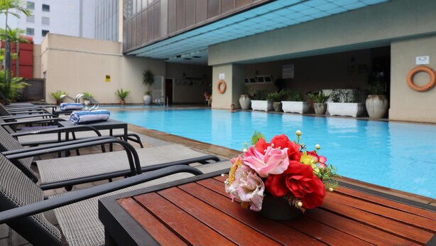 Zona de piscina con sillones, una mesa de madera con un ramo de flores y una piscina azul cristalina.
