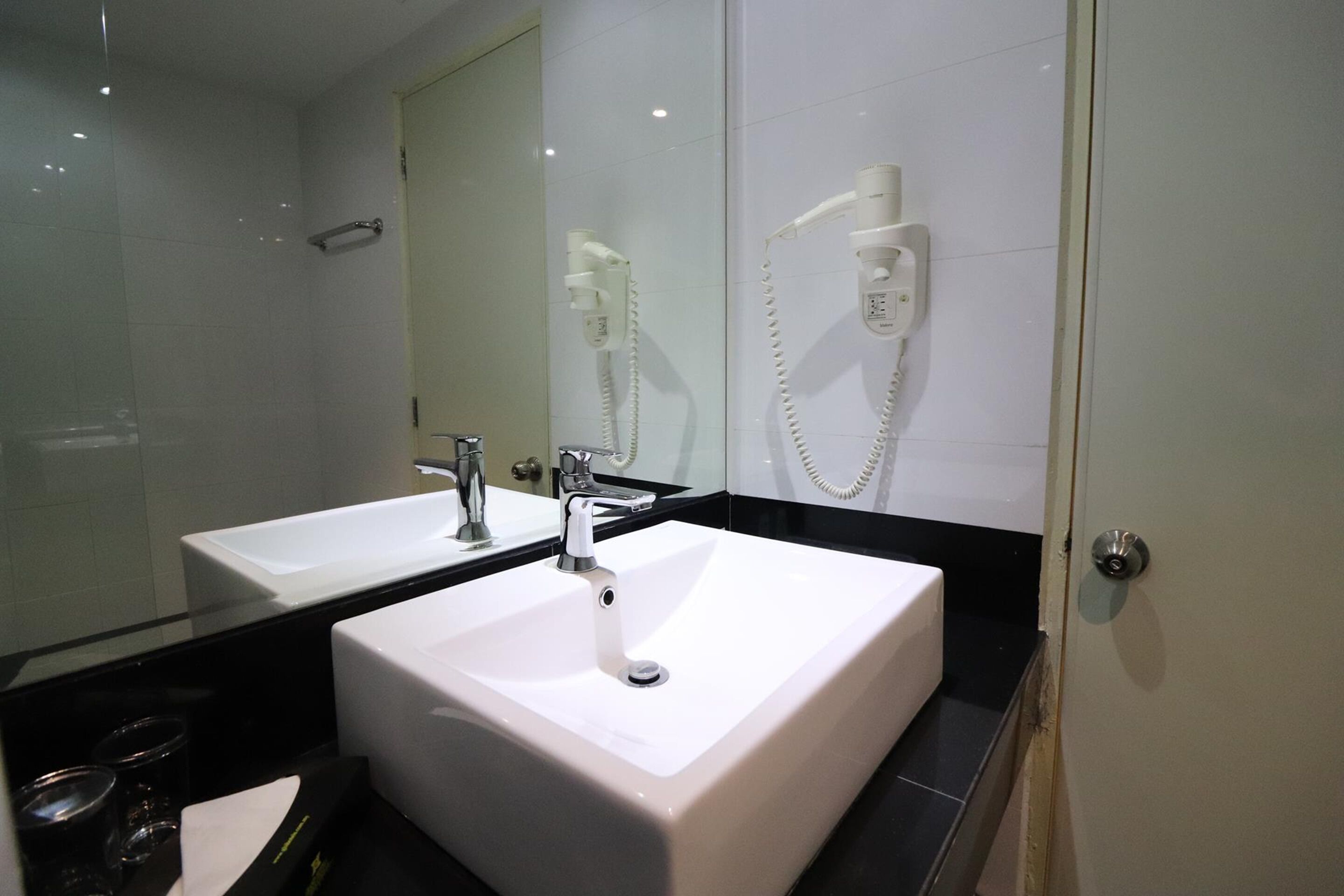 A bathroom with two sinks, a mirror, and a hairdryer mounted on the wall.