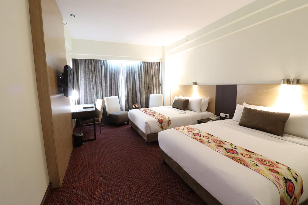 A hotel room with two beds, a desk, a chair, and a TV.