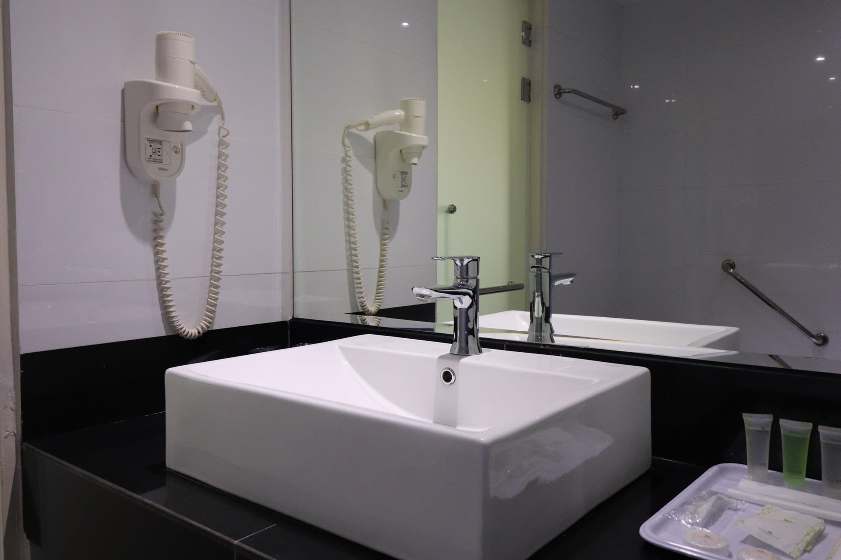 Un baño con un lavamanos blanco, un espejo y un secador de pelo montado en la pared.
