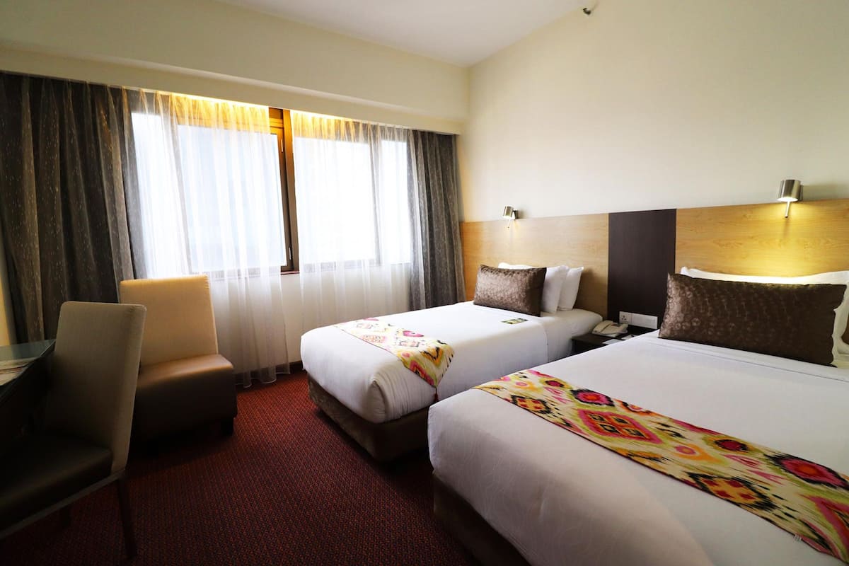 A hotel room with two beds, a desk, a chair, and a large window with curtains.