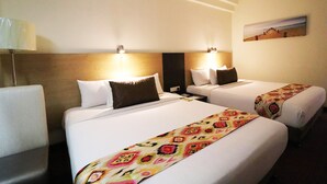 Una habitación de hotel con dos camas, una mesita de noche, una lámpara y un cuadro en la pared.