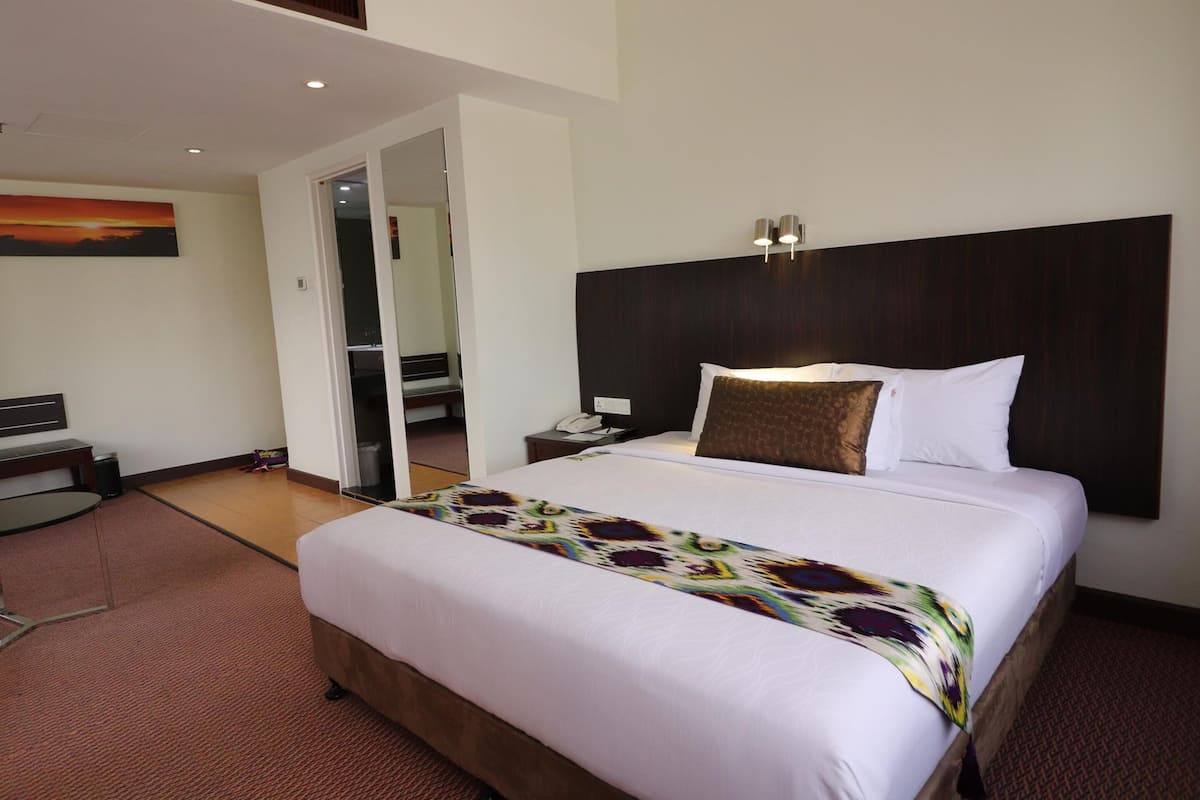 A hotel room with a large bed, a desk, and a door leading to a balcony.