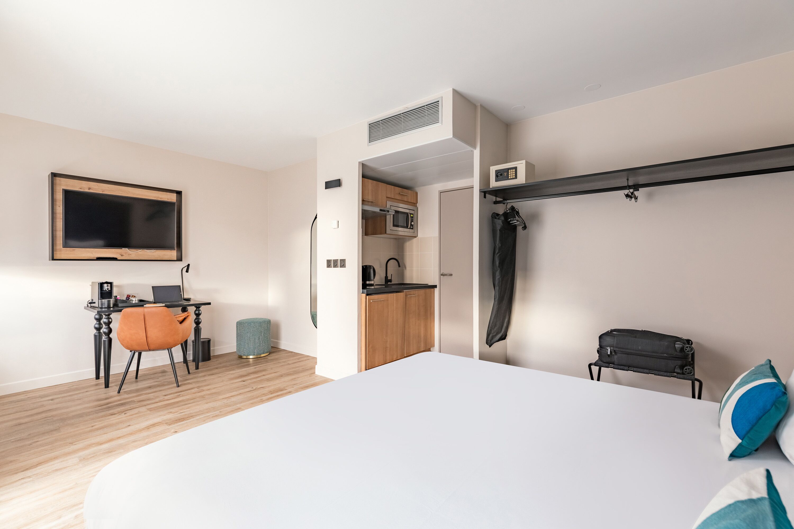 A modern hotel room with a bed, a desk with a laptop, a microwave, and a kitchenette.