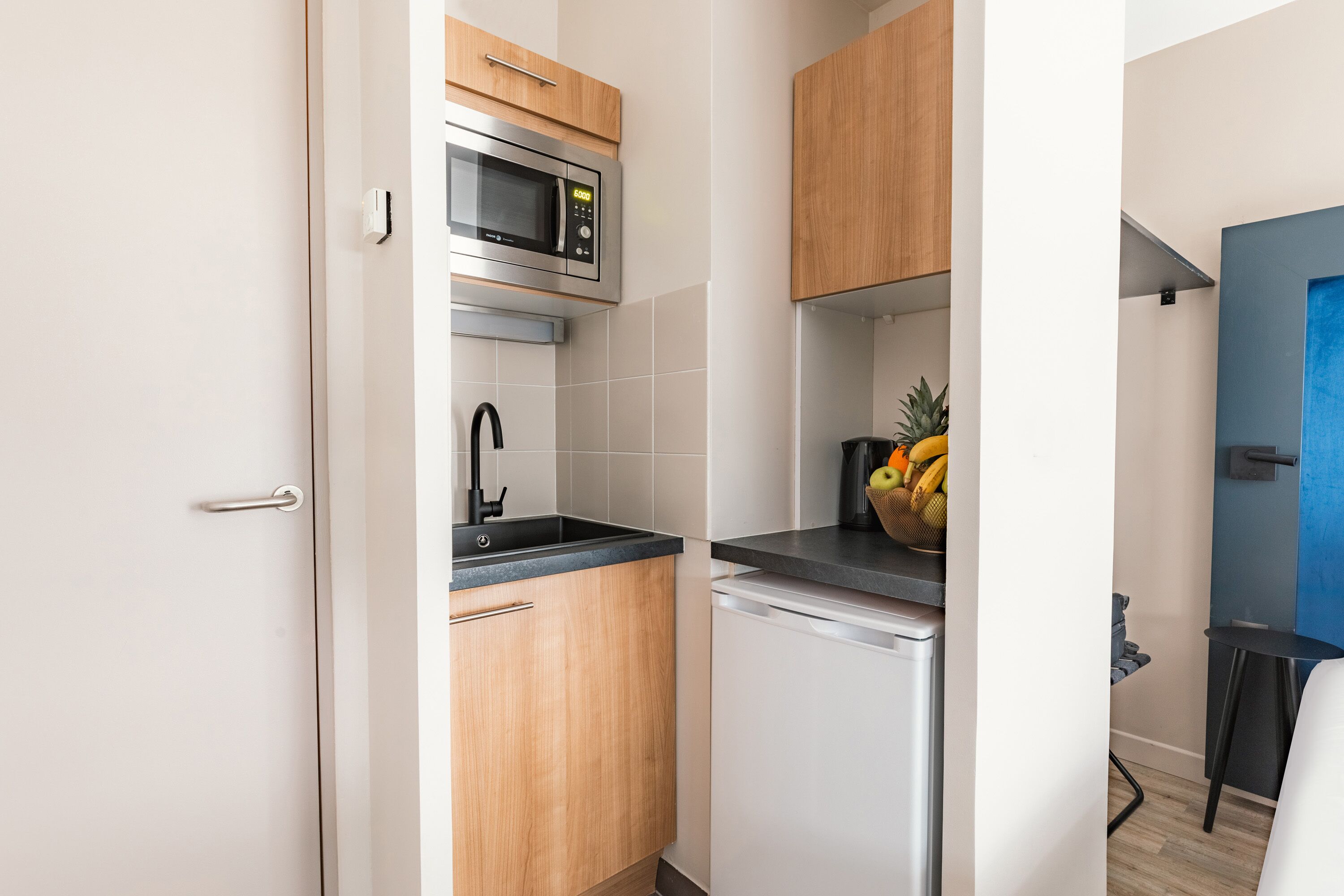 A compact kitchen with wooden cabinets, a stainless steel microwave, and a small refrigerator.