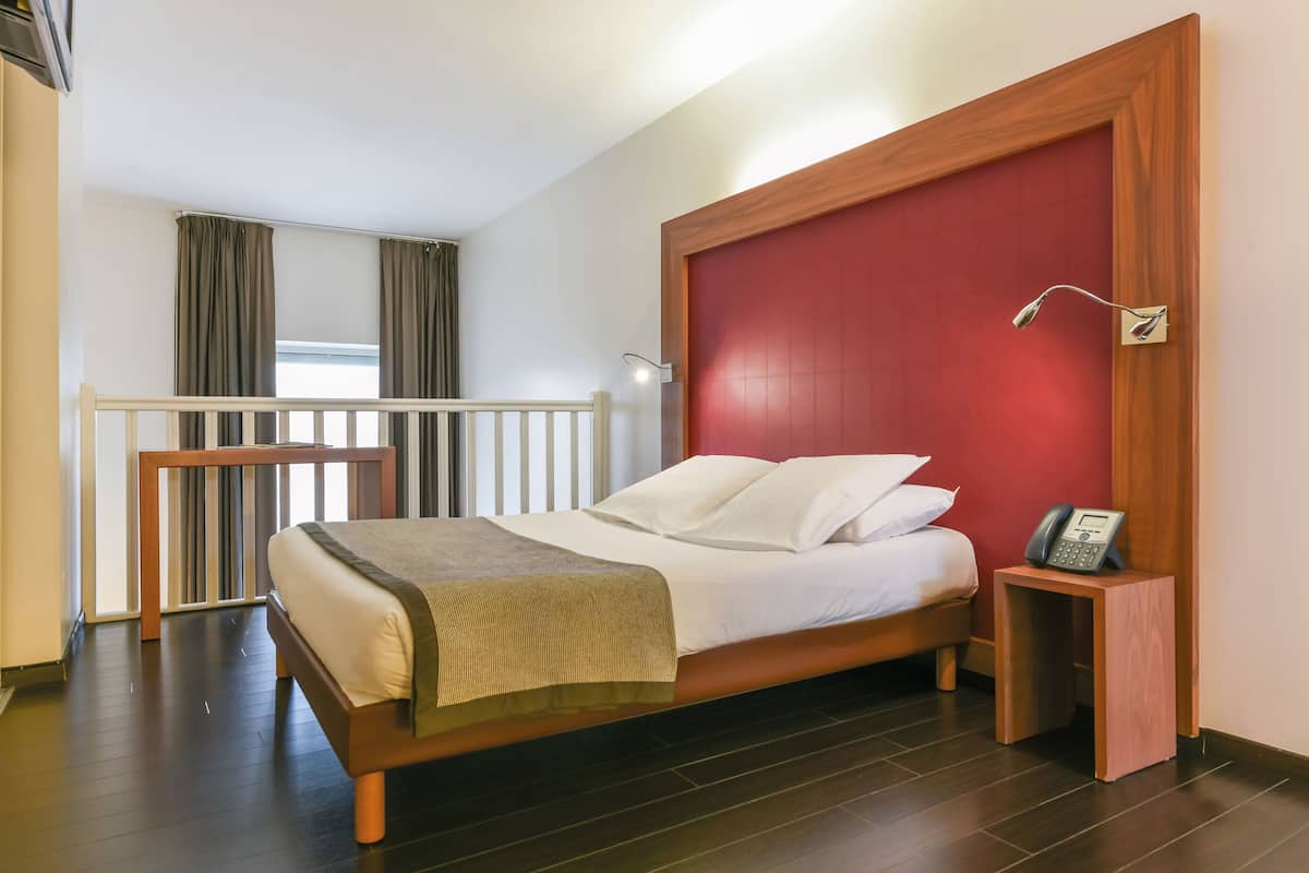 A hotel room with a bed, bedside table, and a small table with a lamp.