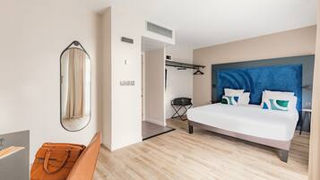 Ein modernes Hotelzimmer mit Bett, Stuhl, Schreibtisch und Kleiderhaken.