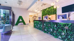 A reception area with a large 'A' decoration, a green wall with plants, a reception desk, and a modern light fixture. - Appart'City Collection Paris Grande Bibliothèque (Paris)