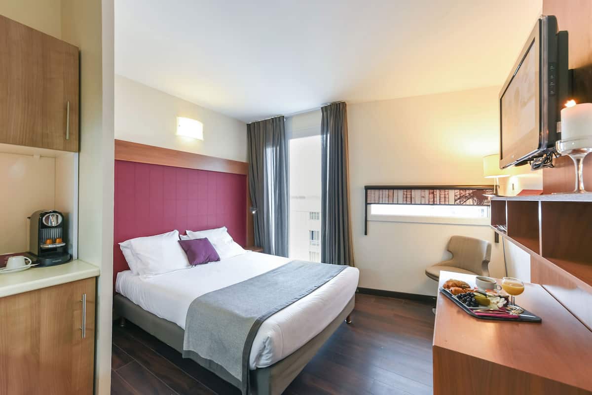 A hotel room with a bed, a desk with a tray of breakfast, a coffee machine, and a TV.