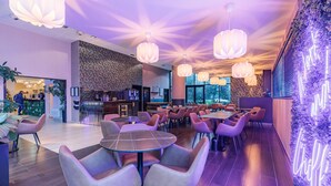 A modern restaurant with round tables and cushioned chairs, a bar area, and a decorative wall with a neon sign. - Appart'City Collection Paris Grande Bibliothèque (Paris)