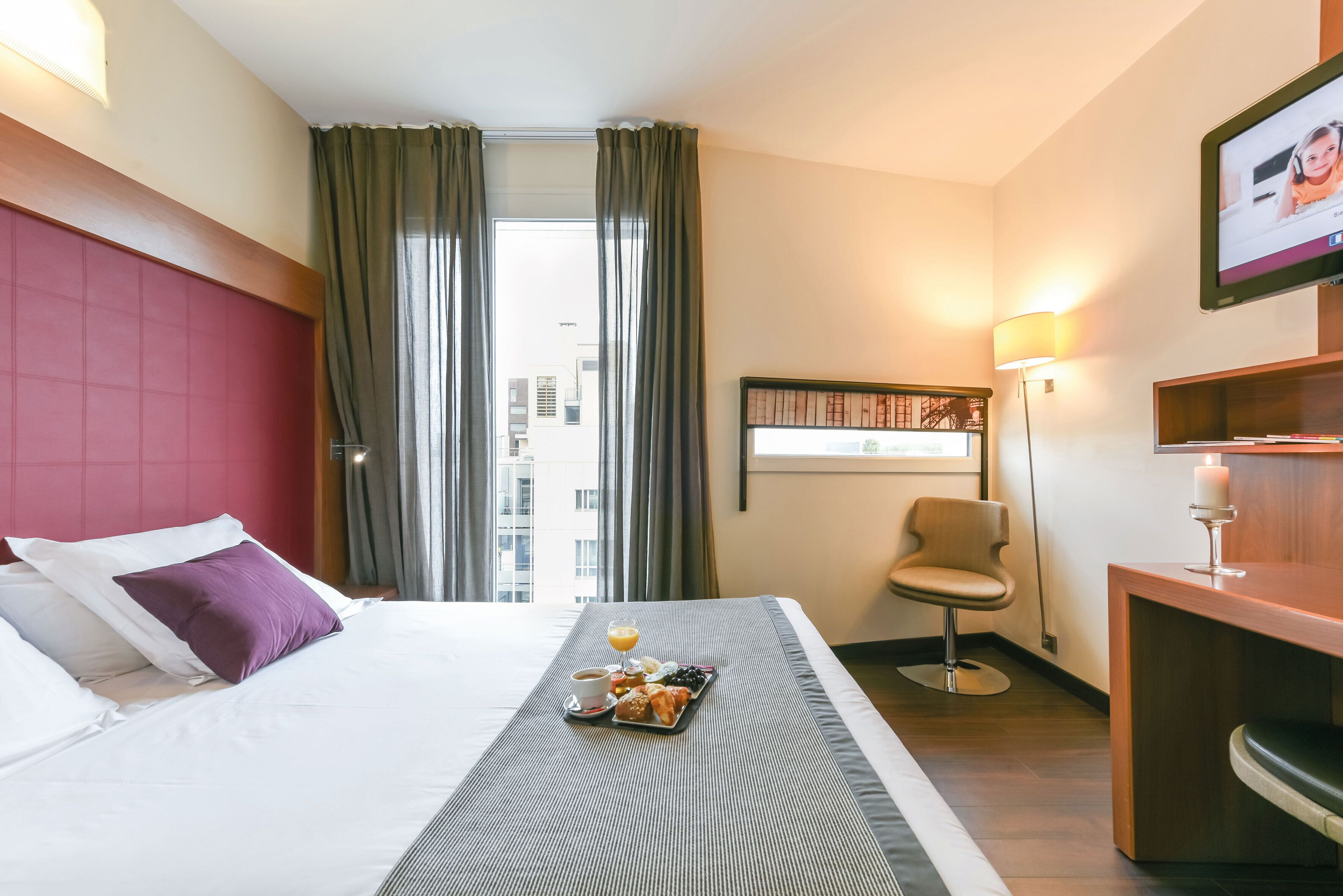 Een hotelkamer met een bed, een ontbijttafel, een bureau, een stoel en uitzicht op de stad.