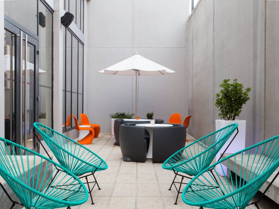 Een terras met stoelen, een tafel, een witte parasol en een plant in pot.