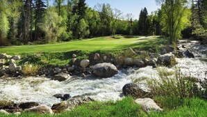 Een golfbaan met een rivier erdoorheen, omgeven door bomen en rotsen.