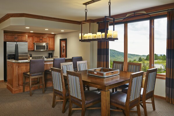 A kitchen with wooden cabinets, a stainless steel refrigerator, and a microwave. There is a dining area with a wooden table and chairs.