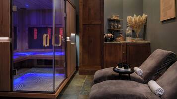 A spa room with a glass-enclosed sauna, a wooden cabinet with decorative items, and a relaxation area with cushioned chairs.