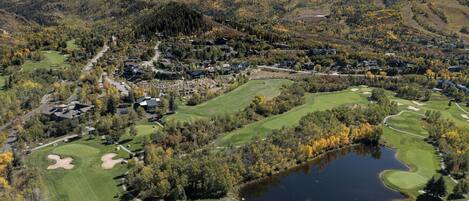 Un parcours de golf avec un étang, entouré d’arbres aux couleurs automnales et de collines en arrière-plan.