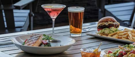 A dining table with a plate of food, a martini glass, a tall beer glass, a burger, fries, and a salad.