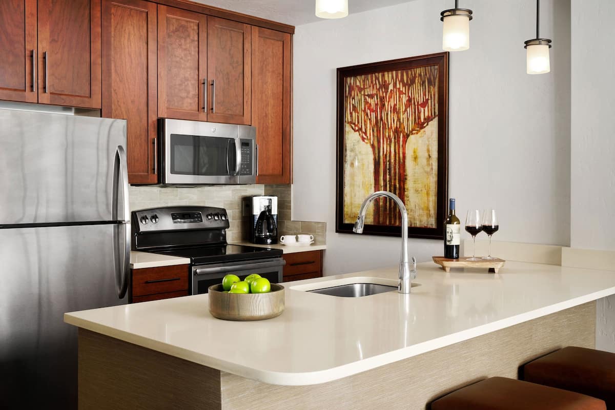 A modern kitchen with stainless steel appliances, wooden cabinets, and a large island with a bowl of green apples.