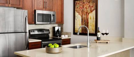 A modern kitchen with stainless steel appliances, wooden cabinets, and a large island with a bowl of green apples.