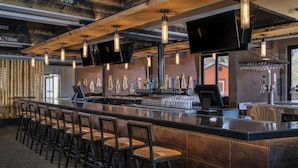 Een bar met een lange toonbank, verschillende barkrukken, een televisie aan het plafond en diverse baraccessoires en tappunten.