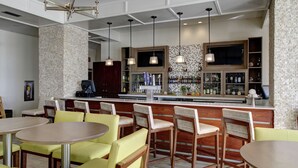 A modern bar area with a brick wall, wooden bar counter, and seating with yellow chairs. - DoubleTree by Hilton Hotel Biloxi (Biloxi)