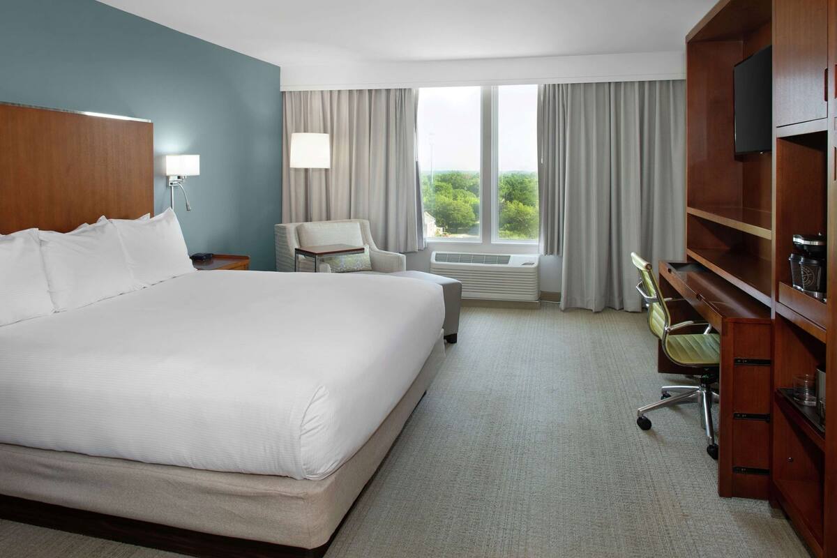 A hotel room with a large bed, a desk, a chair, a TV, and a view of the outdoors.