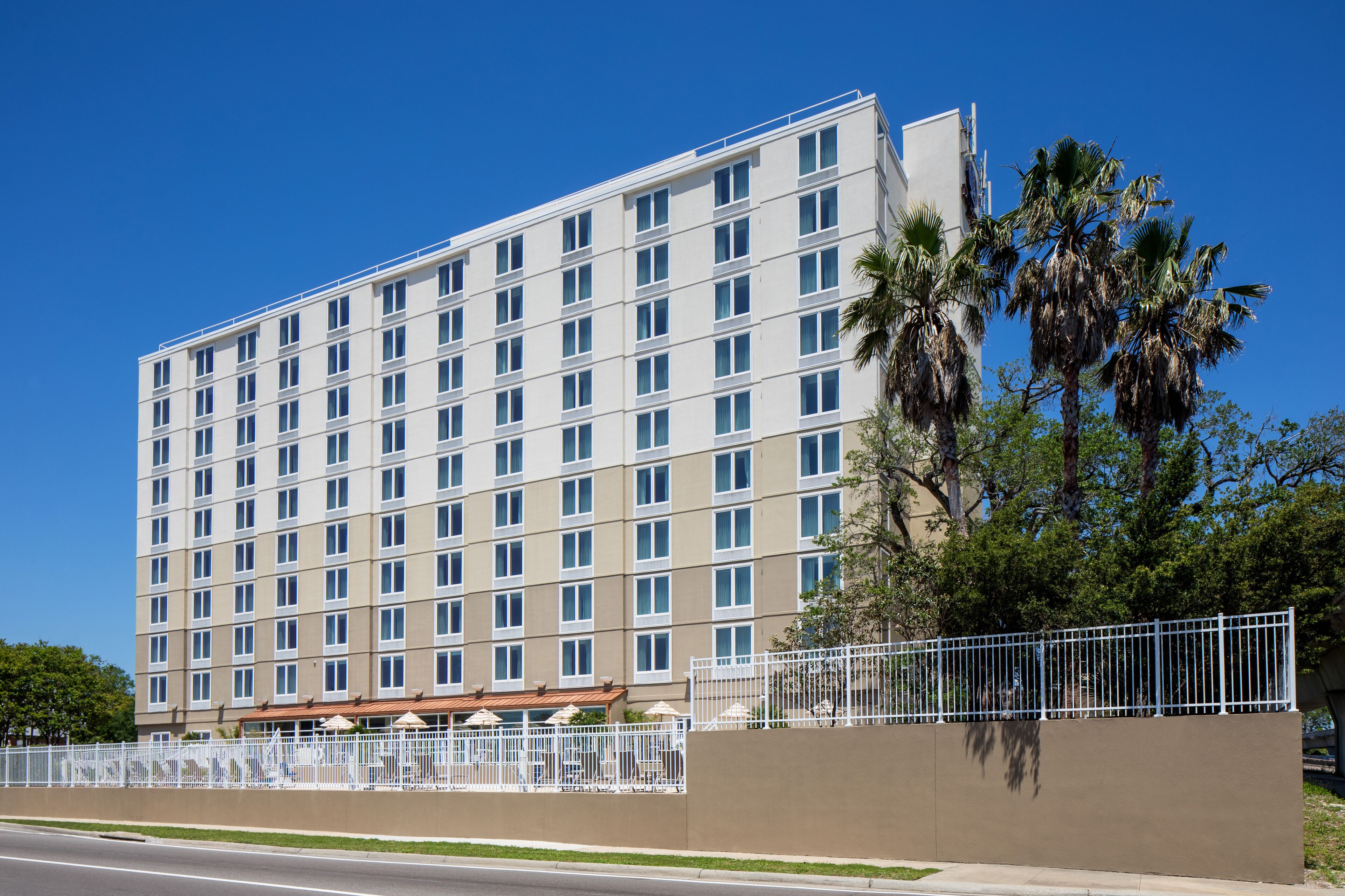 A multi-story hotel with a modern design, featuring a series of balconies and a gated entrance.