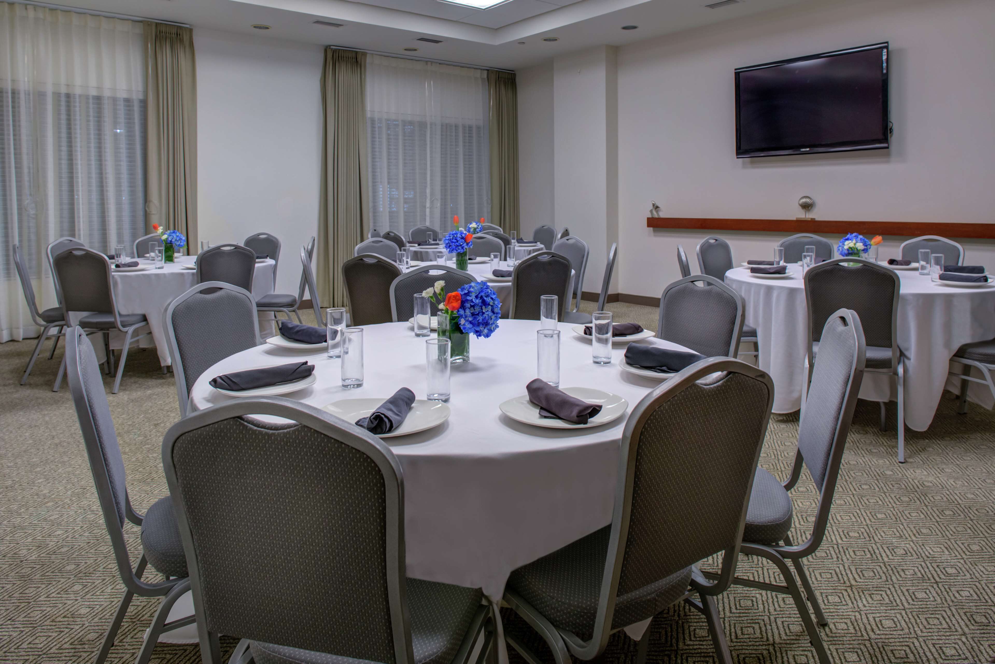 A conference room with round tables, chairs, and a flat-screen TV on the wall.
