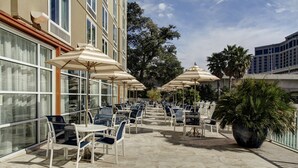 An outdoor patio with multiple tables and chairs, large umbrellas, and a potted plant. - DoubleTree by Hilton Hotel Biloxi (Biloxi)