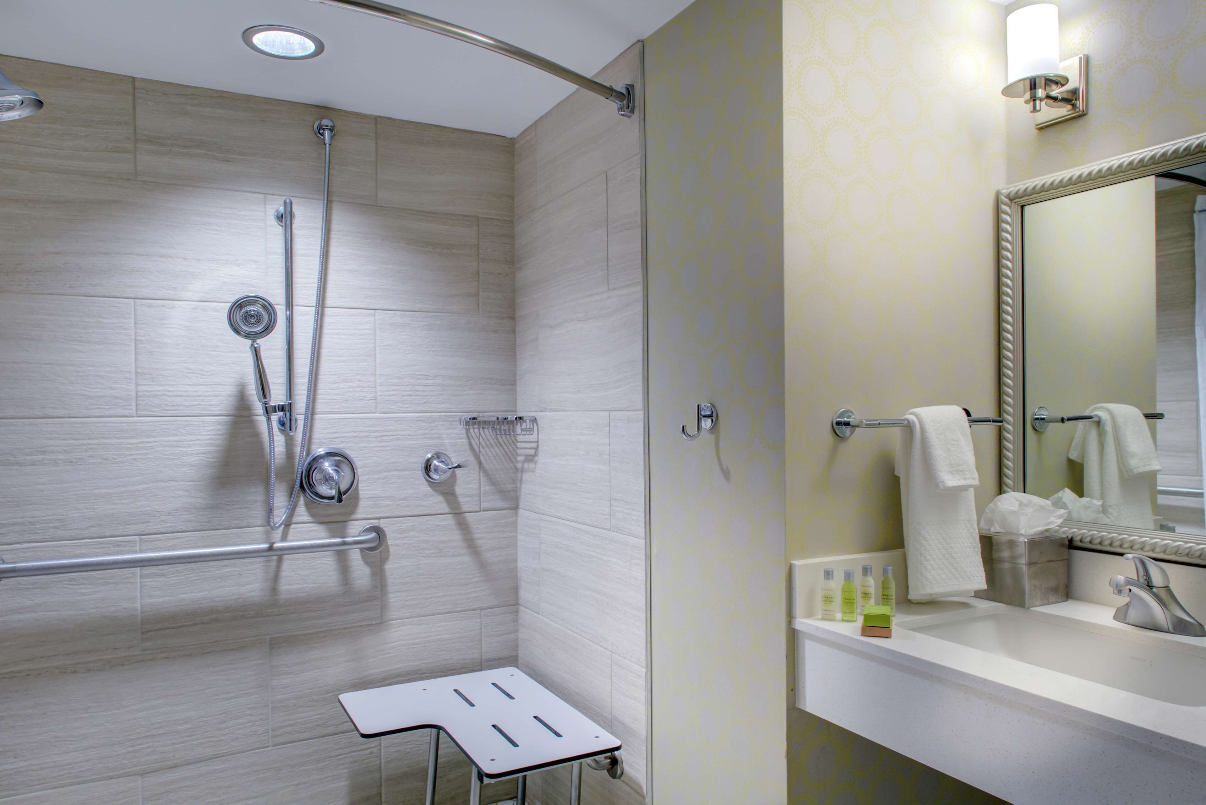 A modern bathroom with a shower, a vanity with a mirror, and a small stool.
