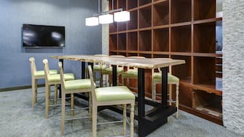 Ein Konferenzraum mit langem Tisch, mehreren Stühlen, einem Flachbildfernseher und einer Holzregalanlage.