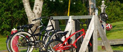 Bicycles parked near a wooden fence with a metal structure, surrounded by greenery.
